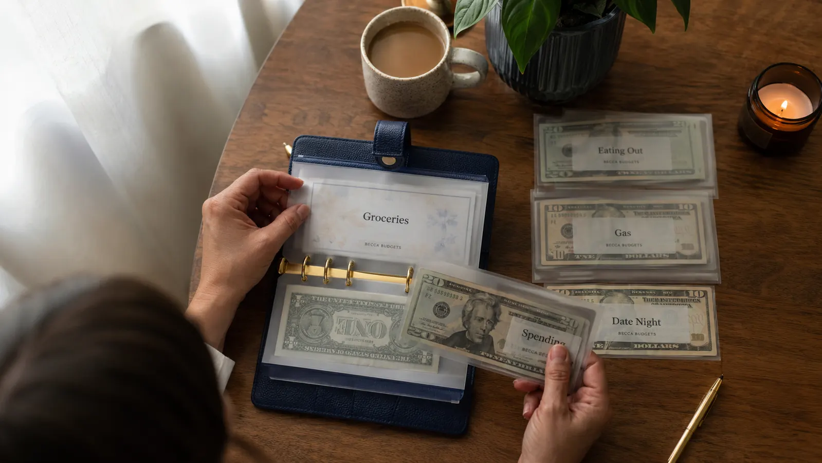 A budget binder open on a kitchen table with labeled cash envelopes fanned out beside a cup of coffee