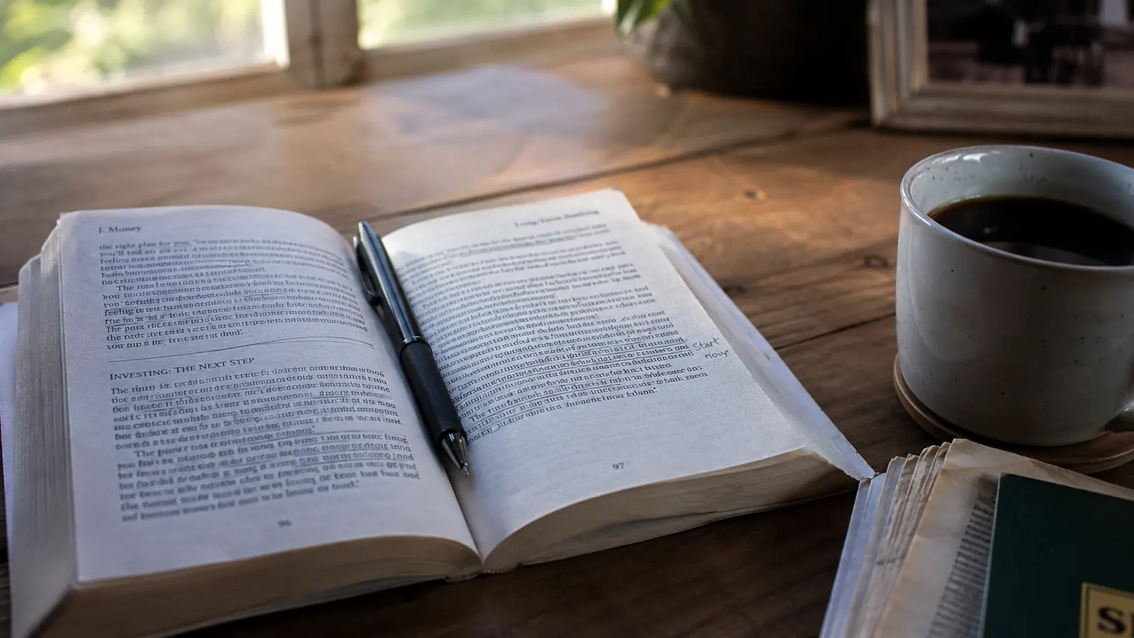 A copy of The Total Money Makeover resting on a desk next to a cup of coffee and a spiral notebook with handwritten budget notes